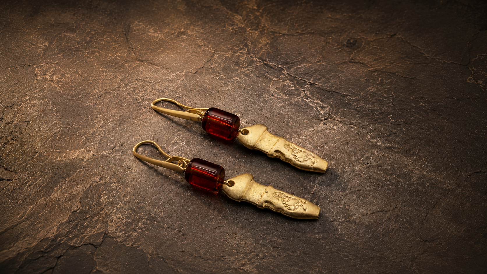Long gold earrings with warm red stones on a dark textured surface