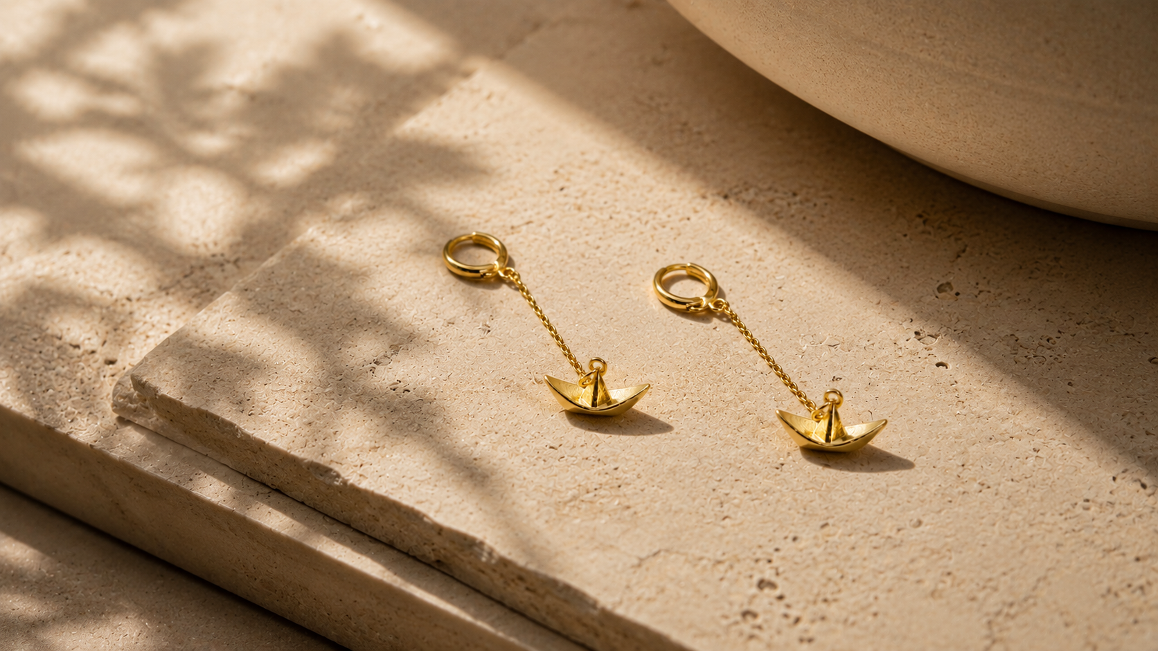 Gold drop earrings on a warm natural stone surface