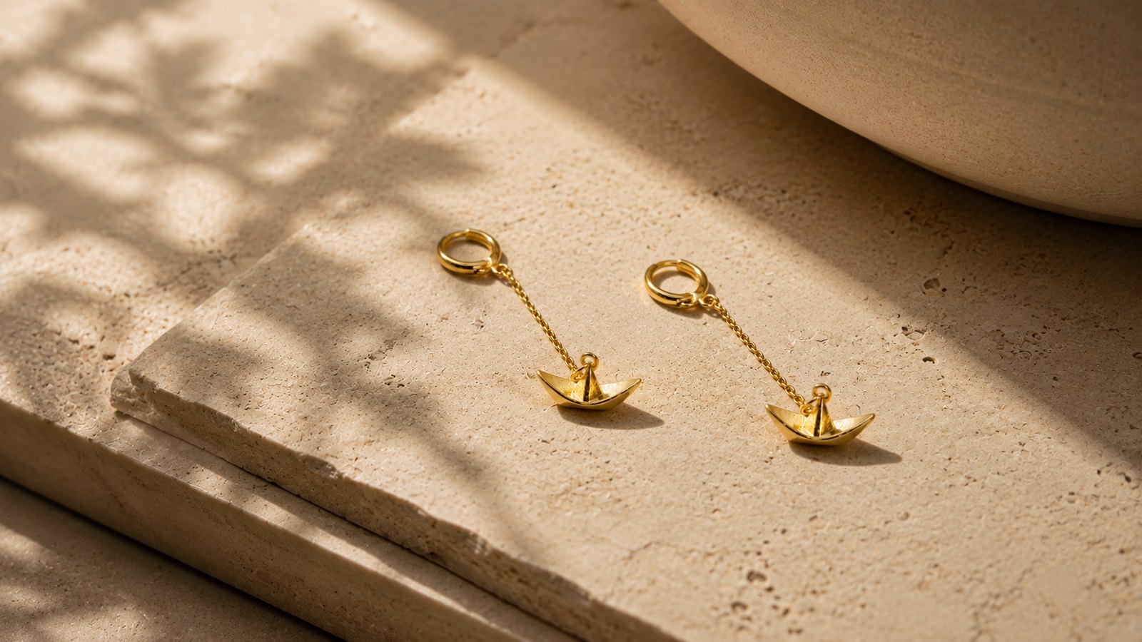 Gold drop earrings on a warm natural stone surface